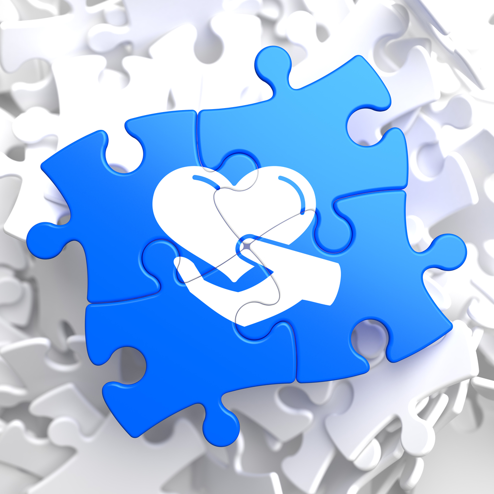 Charity Concept - Icon of Heart in the Hand - Located on Blue Puzzle Pieces. Social Background.